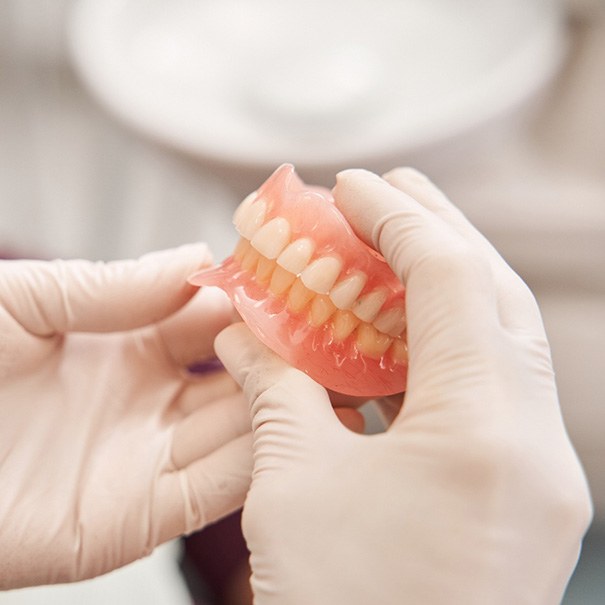 Gloved hands holding a complete set of dentures