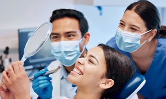 Patient smiling at reflection with dental hygienist and dentist