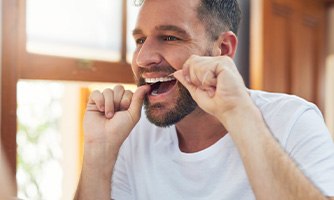 Man smiling while flossing his teeth in bathroom