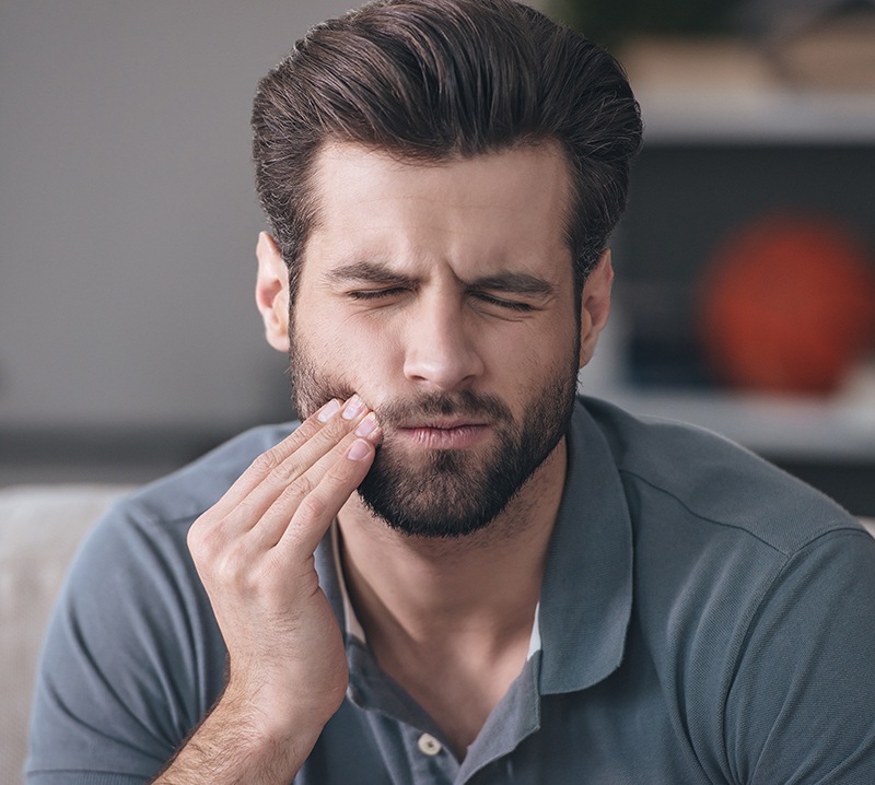 Man in need of emergency dentistry holding his jaw in pain
