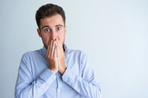 Shocked man with chipped tooth covers his mouth