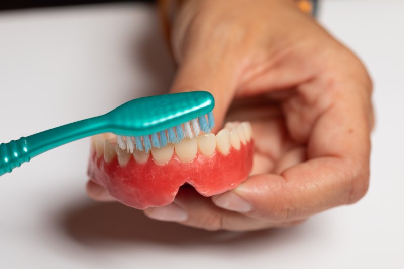person cleaning dentures with toothbrush